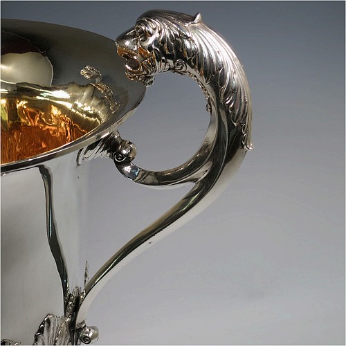 A very large, heavy, and handsome Antique Edwardian Sterling Silver three-handled trophy cup, having a round body with tapering sides and hand-chased half anthemion leaf decoration, with a gold-gilt interior, three cast flying scroll handles with leopard face terminals, and all sitting on a pedestal foot. Made by Goldsmiths and Silversmiths of London in 1905. The dimensions of this fine hand-made large antique silver trophy cup are height 43 cms (17 inches), spread across arms 38 cms (15 inches), and it weighs approx. 3,225g (104 troy ounces).
