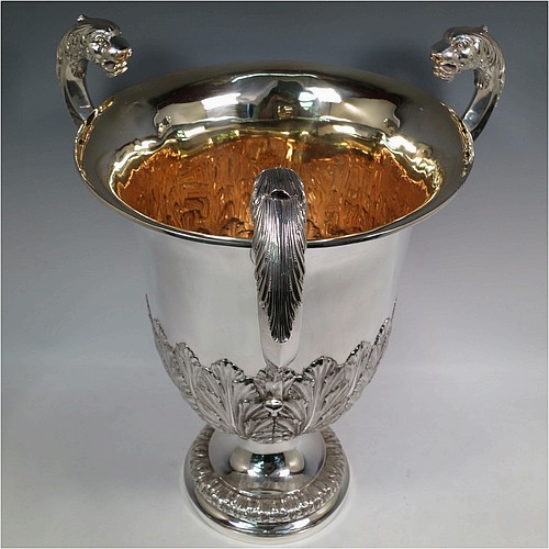 A very large, heavy, and handsome Antique Edwardian Sterling Silver three-handled trophy cup, having a round body with tapering sides and hand-chased half anthemion leaf decoration, with a gold-gilt interior, three cast flying scroll handles with leopard face terminals, and all sitting on a pedestal foot. Made by Goldsmiths and Silversmiths of London in 1905. The dimensions of this fine hand-made large antique silver trophy cup are height 43 cms (17 inches), spread across arms 38 cms (15 inches), and it weighs approx. 3,225g (104 troy ounces).
