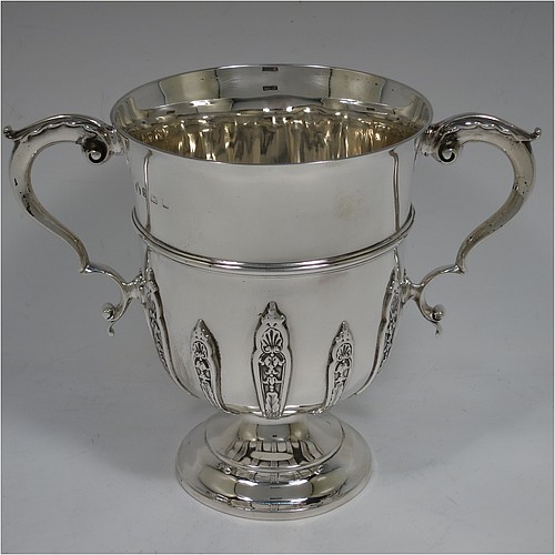 A very handsome Antique Edwardian Sterling Silver trophy cup, in a George II style, having a round body with applied floral strap-work decoration, two scroll side-handles with anthemion leaf thumb-pieces, a central applied girdle band, and all sitting on a stepped pedestal foot. Made by Elkington and Co., of Birmingham in 1908. The dimensions of this fine hand-made antique silver trophy cup are height 16 cms (6.3 inches), spread across arms 21 cms (8.25 inches), and it weighs approx. 510g (16.5 troy ounces).    