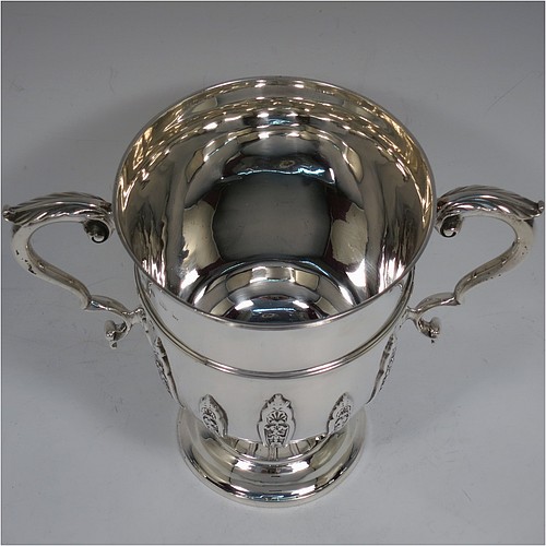 A very handsome Antique Edwardian Sterling Silver trophy cup, in a George II style, having a round body with applied floral strap-work decoration, two scroll side-handles with anthemion leaf thumb-pieces, a central applied girdle band, and all sitting on a stepped pedestal foot. Made by Elkington and Co., of Birmingham in 1908. The dimensions of this fine hand-made antique silver trophy cup are height 16 cms (6.3 inches), spread across arms 21 cms (8.25 inches), and it weighs approx. 510g (16.5 troy ounces).    