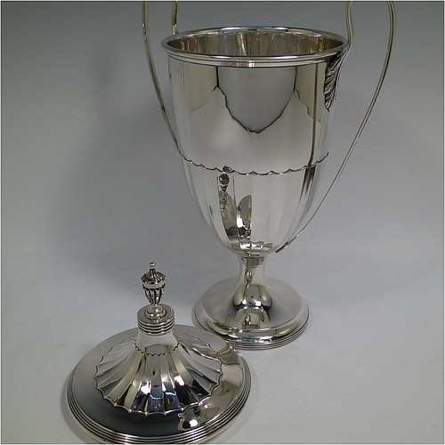 A very handsome Sterling Silver trophy cup and cover in a George III neoclassical style, having a round body with tapering sides and half-fluted decoration, with hand-chased reeded borders, two looped side-handles, an original cover with matching decoration and cast urn finial, and all sitting on a pedestal foot. Made by Robert Pringle of London in 1923. The dimensions of this fine hand-made silver trophy cup and cover are height 33 cms (13 inches), spread across arms 21 cms (8.25 inches), and it weighs approx. 879g (28 troy ounces).