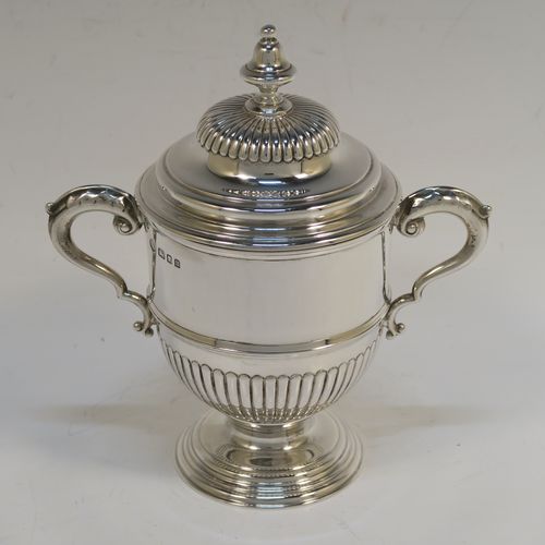 A small but fantastic quality Sterling Silver trophy cup and cover, having a round body with hand-chased half-fluted, with two cast scroll side-handles, a lift-off cover with matching decoration and a cast urn-shaped finial, and all sitting on a stepped pedestal foot. This very handsome silver trophy cup and cover was made by Henry Phillips of London in 1935. The dimensions of this fine hand-made silver trophy cup are height 15 cms (6 inches), spread across handles 14.5 cms (5.75 inches), and it weighs approx. 375g (12 troy ounces).  