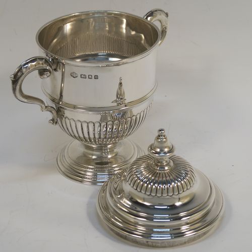 A small but fantastic quality Sterling Silver trophy cup and cover, having a round body with hand-chased half-fluted, with two cast scroll side-handles, a lift-off cover with matching decoration and a cast urn-shaped finial, and all sitting on a stepped pedestal foot. This very handsome silver trophy cup and cover was made by Henry Phillips of London in 1935. The dimensions of this fine hand-made silver trophy cup are height 15 cms (6 inches), spread across handles 14.5 cms (5.75 inches), and it weighs approx. 375g (12 troy ounces).  