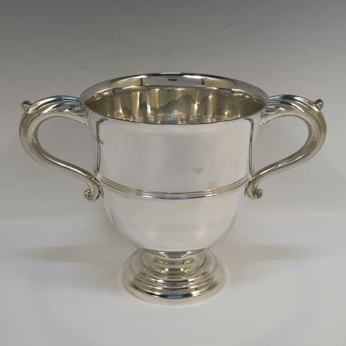 A very handsome Sterling Silver trophy cup in a George III neoclassical style, having a round plain body with tapering sides, an applied central reeded band, two cast scroll side-handles, and all sitting on a stepped pedestal foot. This elegant silver trophy cup was made by Fordham and Faulkner of Sheffield in 1925. The dimensions of this fine hand-made silver trophy cup are height 18 cms (7 inches), spread across arms 27 cms (10.5 inches), and it weighs approx. 620g (20 troy ounces).   