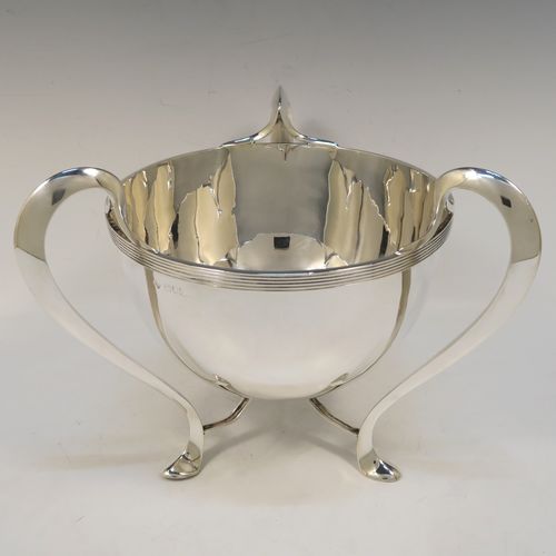 An elegant and heavy Antique Edwardian Sterling Silver three-handled Loving cup bowl, having a plain round body with tapering sides and an applied reeded top border, with three scroll side-handled feet. This handsome antique silver loving cup trophy bowl was made by Horace Woodward of London in 1903. The dimensions of this fine hand-made sterling silver trophy cup bowl are height 21 cms (8.25 inches), diameter of main body 20 cms (8 inches), and it weighs approx. 1,198g (38.6 troy ounces).  