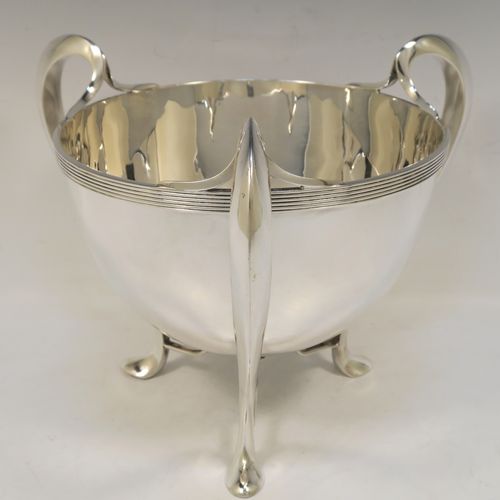 An elegant and heavy Antique Edwardian Sterling Silver three-handled Loving cup bowl, having a plain round body with tapering sides and an applied reeded top border, with three scroll side-handled feet. This handsome antique silver loving cup trophy bowl was made by Horace Woodward of London in 1903. The dimensions of this fine hand-made sterling silver trophy cup bowl are height 21 cms (8.25 inches), diameter of main body 20 cms (8 inches), and it weighs approx. 1,198g (38.6 troy ounces).  