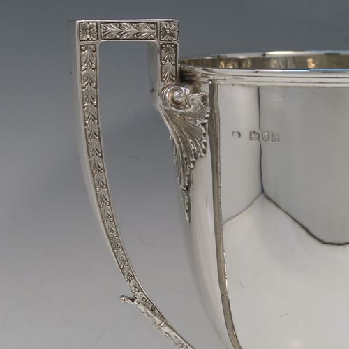 A large and handsome Antique Victorian Sterling Silver trophy cup in a George III neoclassical style, having a plain round body with tapering sides, two cast flat-topped side-handles with hand-chased oak-leaf decoration, and all sitting on a plain round stepped pedestal foot. This handsome silver trophy cup was made by Charles Boyton of London in 1898. The dimensions of this fine hand-made antique silver trophy cup are height 32 cms (12.5 inches), spread across arms 26.5 cms (10.5 inches), and it weighs approx. 1,232g (39.7 troy ounces).   
