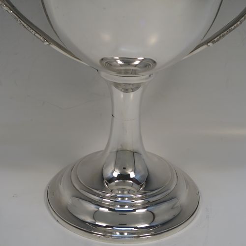 A large and handsome Antique Victorian Sterling Silver trophy cup in a George III neoclassical style, having a plain round body with tapering sides, two cast flat-topped side-handles with hand-chased oak-leaf decoration, and all sitting on a plain round stepped pedestal foot. This handsome silver trophy cup was made by Charles Boyton of London in 1898. The dimensions of this fine hand-made antique silver trophy cup are height 32 cms (12.5 inches), spread across arms 26.5 cms (10.5 inches), and it weighs approx. 1,232g (39.7 troy ounces).   