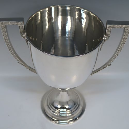 A large and handsome Antique Victorian Sterling Silver trophy cup in a George III neoclassical style, having a plain round body with tapering sides, two cast flat-topped side-handles with hand-chased oak-leaf decoration, and all sitting on a plain round stepped pedestal foot. This handsome silver trophy cup was made by Charles Boyton of London in 1898. The dimensions of this fine hand-made antique silver trophy cup are height 32 cms (12.5 inches), spread across arms 26.5 cms (10.5 inches), and it weighs approx. 1,232g (39.7 troy ounces).   