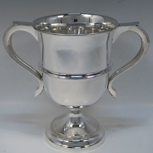 A very handsome Sterling Silver trophy cup in a George III neoclassical style, having a round plain body with tapering sides, an applied central reeded band, two plain scroll side-handles, and all sitting on a stepped pedestal foot. This elegant silver trophy cup was made by Carrington and Co., of Birmingham in 1931. The dimensions of this fine hand-made silver trophy cup are height 21 cms (8.25 inches), spread across arms 23.5 cms (9.25 inches), and it weighs approx. 715g (23 troy ounces).  