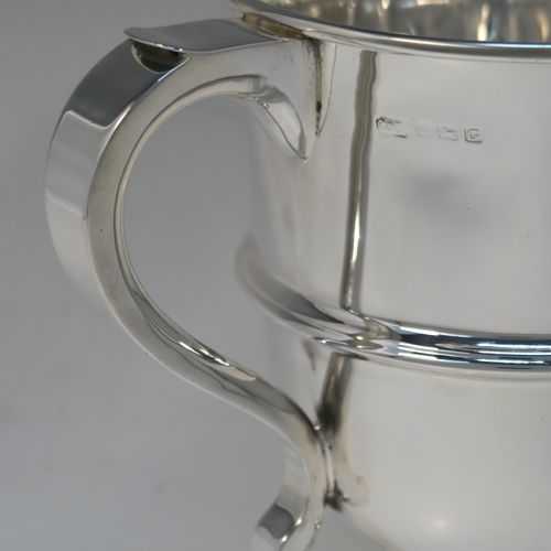 A very handsome Sterling Silver trophy cup in a George III neoclassical style, having a round plain body with tapering sides, an applied central reeded band, two plain scroll side-handles, and all sitting on a stepped pedestal foot. This elegant silver trophy cup was made by Carrington and Co., of Birmingham in 1931. The dimensions of this fine hand-made silver trophy cup are height 21 cms (8.25 inches), spread across arms 23.5 cms (9.25 inches), and it weighs approx. 715g (23 troy ounces).  