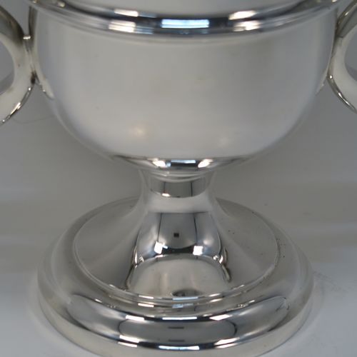 A very handsome Sterling Silver trophy cup in a George III neoclassical style, having a round plain body with tapering sides, an applied central reeded band, two plain scroll side-handles, and all sitting on a stepped pedestal foot. This elegant silver trophy cup was made by Carrington and Co., of Birmingham in 1931. The dimensions of this fine hand-made silver trophy cup are height 21 cms (8.25 inches), spread across arms 23.5 cms (9.25 inches), and it weighs approx. 715g (23 troy ounces).  