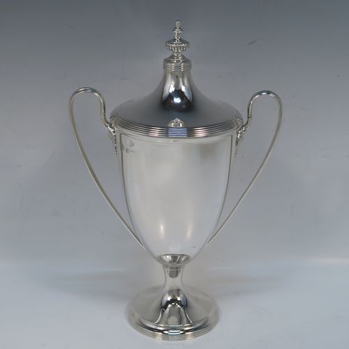 A very handsome Antique Edwardian Sterling Silver trophy cup and cover in a George III neoclassical style, having a round plain body with tapering sides, with hand-chased reeded borders, two looped side-handles, an original cover with matching decoration and cast knop finial, and all sitting on a pedestal foot. This beautiful silver trophy cup was made by Elkington and Co., of Birmingham in 1908. The dimensions of this fine hand-made silver trophy cup and cover are height 24 cms (9.5 inches), spread across arms 16.5 cms (6.5 inches), and it weighs approx. 387g (12.5 troy ounces).   