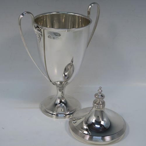 A very handsome Antique Edwardian Sterling Silver trophy cup and cover in a George III neoclassical style, having a round plain body with tapering sides, with hand-chased reeded borders, two looped side-handles, an original cover with matching decoration and cast knop finial, and all sitting on a pedestal foot. This beautiful silver trophy cup was made by Elkington and Co., of Birmingham in 1908. The dimensions of this fine hand-made silver trophy cup and cover are height 24 cms (9.5 inches), spread across arms 16.5 cms (6.5 inches), and it weighs approx. 387g (12.5 troy ounces).