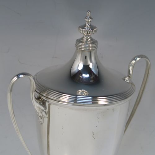 A very handsome Antique Edwardian Sterling Silver trophy cup and cover in a George III neoclassical style, having a round plain body with tapering sides, with hand-chased reeded borders, two looped side-handles, an original cover with matching decoration and cast knop finial, and all sitting on a pedestal foot. This beautiful silver trophy cup was made by Elkington and Co., of Birmingham in 1908. The dimensions of this fine hand-made silver trophy cup and cover are height 24 cms (9.5 inches), spread across arms 16.5 cms (6.5 inches), and it weighs approx. 387g (12.5 troy ounces).