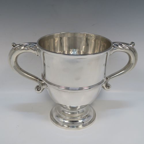 A very handsome Antique Edwardian Sterling Silver trophy cup in a George III style, having a plain round bellied body, with an applied reeded girdle, two scroll side-handles with anthemion leaf thumb-pieces, and all sitting on a round pedestal foot. This elegant antique sterling silver trophy cup was made by Gibson and Co., of London in 1908. The dimensions of this fine hand-made silver trophy cup are height 21 cms (8.25 inches), spread across arms 31.5 cms (12.3 inches), and it weighs approx. 899g (29 troy ounces).   