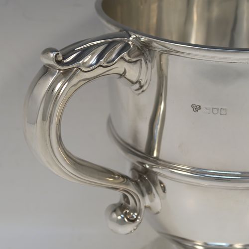 A very handsome Antique Edwardian Sterling Silver trophy cup in a George III style, having a plain round bellied body, with an applied reeded girdle, two scroll side-handles with anthemion leaf thumb-pieces, and all sitting on a round pedestal foot. This elegant antique sterling silver trophy cup was made by Gibson and Co., of London in 1908. The dimensions of this fine hand-made silver trophy cup are height 21 cms (8.25 inches), spread across arms 31.5 cms (12.3 inches), and it weighs approx. 899g (29 troy ounces).
