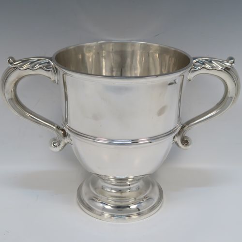 A very handsome Antique Edwardian Sterling Silver trophy cup in a George III style, having a plain round bellied body, with an applied reeded girdle, two scroll side-handles with anthemion leaf thumb-pieces, and all sitting on a round pedestal foot. This elegant antique sterling silver trophy cup was made by Gibson and Co., of London in 1908. The dimensions of this fine hand-made silver trophy cup are height 21 cms (8.25 inches), spread across arms 31.5 cms (12.3 inches), and it weighs approx. 899g (29 troy ounces).