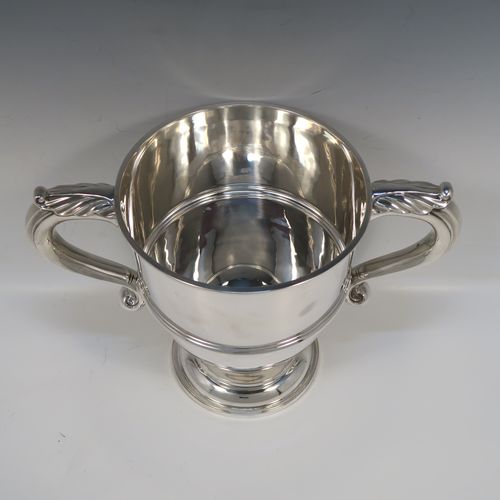 A very handsome Antique Edwardian Sterling Silver trophy cup in a George III style, having a plain round bellied body, with an applied reeded girdle, two scroll side-handles with anthemion leaf thumb-pieces, and all sitting on a round pedestal foot. This elegant antique sterling silver trophy cup was made by Gibson and Co., of London in 1908. The dimensions of this fine hand-made silver trophy cup are height 21 cms (8.25 inches), spread across arms 31.5 cms (12.3 inches), and it weighs approx. 899g (29 troy ounces).