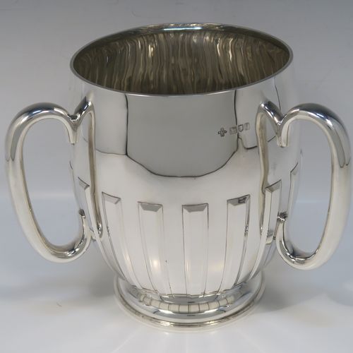 A large and handsome Antique Edwardian Sterling Silver three-handled Loving cup trophy, having a plain round bellied body with hand-chased rectangular style half-fluted decoration, together with three loop side handles, and all sitting on a round pedestal foot. This elegant silver loving cup trophy was made by Henry Woodward and Co., of London in 1902. The dimensions of this fine hand-made antique sterling silver trophy cup are height 19 cms (7.5 inches), diameter of main body 16.5 cms (6.5 inches), and it weighs approx. 844g (27 troy ounces).   