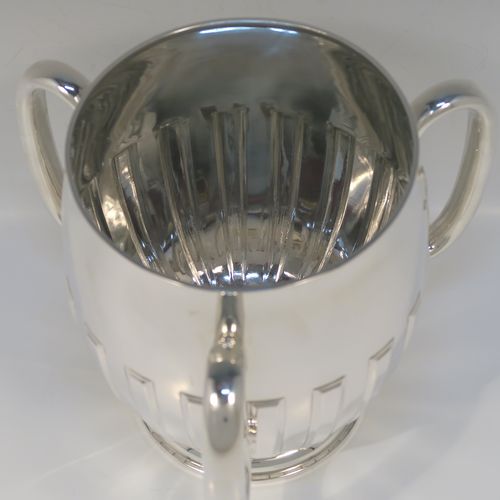 A large and handsome Antique Edwardian Sterling Silver three-handled Loving cup trophy, having a plain round bellied body with hand-chased rectangular style half-fluted decoration, together with three loop side handles, and all sitting on a round pedestal foot. This elegant silver loving cup trophy was made by Henry Woodward and Co., of London in 1902. The dimensions of this fine hand-made antique sterling silver trophy cup are height 19 cms (7.5 inches), diameter of main body 16.5 cms (6.5 inches), and it weighs approx. 844g (27 troy ounces).   