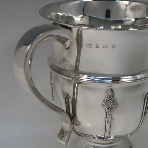 A very handsome Antique Sterling Silver trophy cup, in a George II style, having a round body with applied floral strap-work decoration, two plain scroll side-handles, a central applied girdle band, and all sitting on a stepped pedestal foot. This elegant silver trophy cup was made by Carrington and Co., of Birmingham in 1924. The dimensions of this fine hand-made antique silver trophy cup are height 20 cms (8 inches), spread across arms 27 cms (10.5 inches), and it weighs approx. 801g (25.8 troy ounces).   