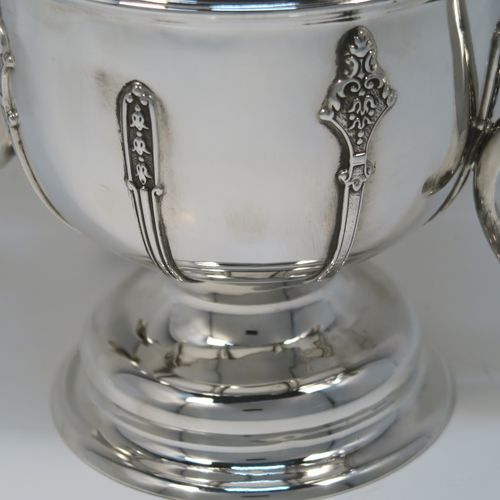 A very handsome Antique Sterling Silver trophy cup, in a George II style, having a round body with applied floral strap-work decoration, two plain scroll side-handles, a central applied girdle band, and all sitting on a stepped pedestal foot. This elegant silver trophy cup was made by Carrington and Co., of Birmingham in 1924. The dimensions of this fine hand-made antique silver trophy cup are height 20 cms (8 inches), spread across arms 27 cms (10.5 inches), and it weighs approx. 801g (25.8 troy ounces).   