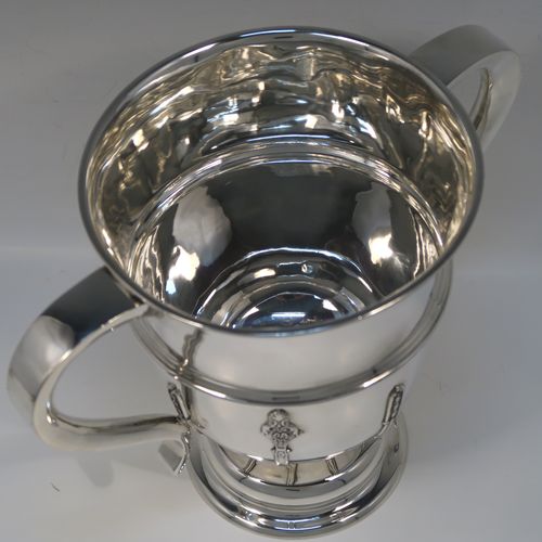 A very handsome Antique Sterling Silver trophy cup, in a George II style, having a round body with applied floral strap-work decoration, two plain scroll side-handles, a central applied girdle band, and all sitting on a stepped pedestal foot. This elegant silver trophy cup was made by Carrington and Co., of Birmingham in 1924. The dimensions of this fine hand-made antique silver trophy cup are height 20 cms (8 inches), spread across arms 27 cms (10.5 inches), and it weighs approx. 801g (25.8 troy ounces).   