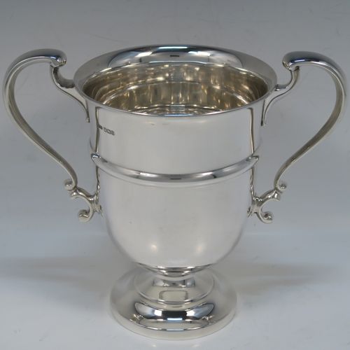 A very handsome Antique Sterling Silver trophy cup in a George III neoclassical style, having a round plain body with tapering sides and a tucked under belly, an applied central reeded band, two plain scroll side-handles, and all sitting on a stepped pedestal foot. This elegant silver trophy cup was made by George Harding and Sons of Sheffield in 1913. The dimensions of this fine hand-made silver trophy cup are height 17 cms (6.75 inches), spread across arms 20 cms (8 inches), and it weighs approx. 412g (13.3 troy ounces).   