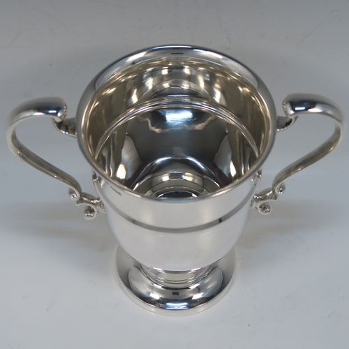A very handsome Antique Sterling Silver trophy cup in a George III neoclassical style, having a round plain body with tapering sides and a tucked under belly, an applied central reeded band, two plain scroll side-handles, and all sitting on a stepped pedestal foot. This elegant silver trophy cup was made by George Harding and Sons of Sheffield in 1913. The dimensions of this fine hand-made silver trophy cup are height 17 cms (6.75 inches), spread across arms 20 cms (8 inches), and it weighs approx. 412g (13.3 troy ounces).