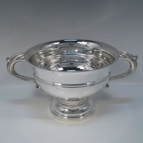 A very handsome Antique Sterling Silver trophy cup, having a plain round bellied body, with two scroll Anthemion leaf side-handles, with a central double-reeded girdle, and all sitting on a round pedestal foot. This elegant antique sterling silver trophy cup was made by Walker and Hall of Sheffield in 1919. The dimensions of this fine hand-made silver trophy cup bowl are height 15 cms (6 inches), spread across arms 31 cms (12.25 inches), and it weighs approx. 729g (23.5 troy ounces).  