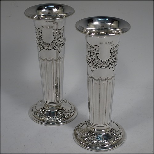 A very pretty Antique Victorian Sterling Silver pair of table flower vases, having round bodies with tapering sides and hand-chased neoclassical style decoration with half-fluting, ribbon bows, and swags, and sitting on pedestal feet. Made by Henry Atkins of Sheffield in 1892. The dimensions of these fine hand-made antique silver pair of vases are height 15 cms (6 inches), diameter at top 6.5 cms (2.5 inches), and they weigh at total of approx. 200g (6.5 troy ounces). Please note that these vases are not loaded.    