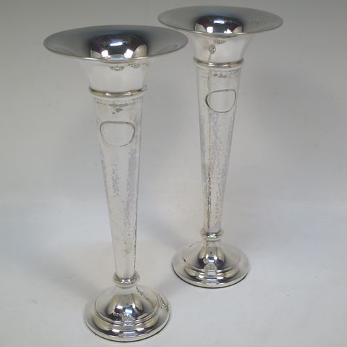 A handsome and stylish Antique Sterling Silver pair of table flower vases, having plain round tops, tapering bodies with hand-hammered decoration and oval vacant cartouches, and sitting on round stepped pedestal bases. Made by Walker and Hall of Sheffield in 1919. The dimensions of these fine hand-made pair of antique silver vases are height 22 cms (8.5 inches), and diameter at top 9 cms (3.5 inches).   