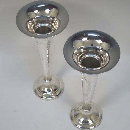 A handsome and stylish Antique Sterling Silver pair of table flower vases, having plain round tops, tapering bodies with hand-hammered decoration and oval vacant cartouches, and sitting on round stepped pedestal bases. Made by Walker and Hall of Sheffield in 1919. The dimensions of these fine hand-made pair of antique silver vases are height 22 cms (8.5 inches), and diameter at top 9 cms (3.5 inches).