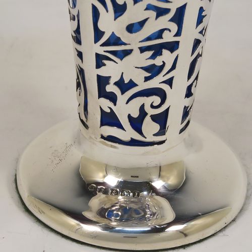 A vert pretty pair of Antique Edwardian Sterling Silver vases, having hand-pierced bodies with floral decoration on round tapering sides, with removable blue-glass liners, with wavy-edge rims and four scroll handles, and all sitting on plain round pedestal feet. These beautiful antique silver vases were made by Harrison and Hipwood of Birmingham in 1910. The dimensions of this fine hand-made pair of antique silver vases are height 13 cms (5.25 inches), and diameter at top 10 cms (4 inches).   