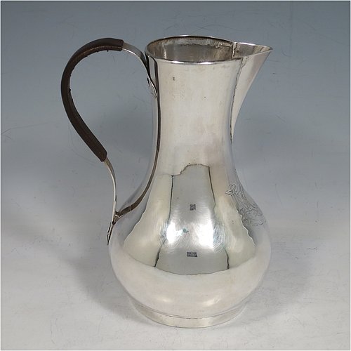 An Antique Georgian Sterling Silver George II very unwater jug, having a plain round bellied body, a sparrow-beak spout, a riveted scroll handle with leather cover, and sitting on a collet foot. Made by William Cripps (possibly) of London in 1755. The dimensions of this fine hand-made antique silver water jug are height 17 cms (6.75 inches), length 13 cms (5 inches), and it weighs approx. 250g (8 troy ounces). Please note that this item is crested.   