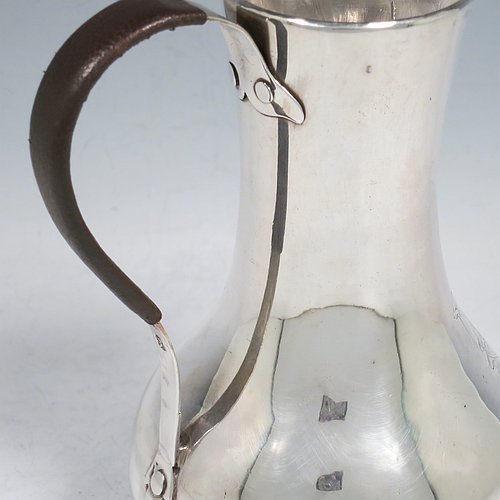 An Antique Georgian Sterling Silver George II very unwater jug, having a plain round bellied body, a sparrow-beak spout, a riveted scroll handle with leather cover, and sitting on a collet foot. Made by William Cripps (possibly) of London in 1755. The dimensions of this fine hand-made antique silver water jug are height 17 cms (6.75 inches), length 13 cms (5 inches), and it weighs approx. 250g (8 troy ounces). Please note that this item is crested.