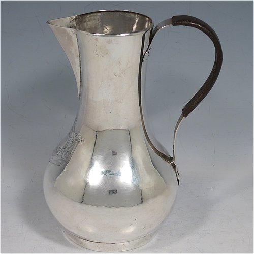 An Antique Georgian Sterling Silver George II very unwater jug, having a plain round bellied body, a sparrow-beak spout, a riveted scroll handle with leather cover, and sitting on a collet foot. Made by William Cripps (possibly) of London in 1755. The dimensions of this fine hand-made antique silver water jug are height 17 cms (6.75 inches), length 13 cms (5 inches), and it weighs approx. 250g (8 troy ounces). Please note that this item is crested.