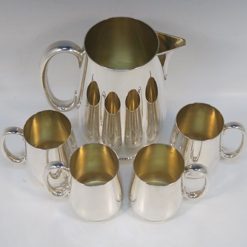 A very handsome Antique Edwardian Silver-Plated water jug with four mugs, in a very plain style, having round bellied bodies with tapering sides, a sparrow-beak spout, scroll side-handles, gold-gilt interiors, and all sitting on collet feet. This antique silver-plated water jug serving set was made in ca. 1900 by Martin Hall and Co., of Sheffield. The dimensions of this fine hand-made silver-plated water jug are height 20 cms (8 inches), and height of mugs are 10 cms (4 inches).