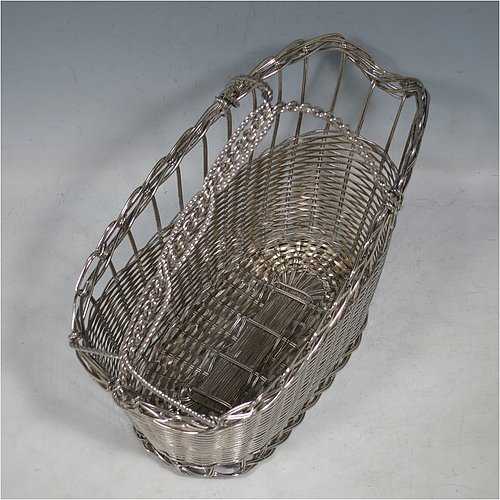 An Antique Victorian Silver Plated wine bottle cradle or holder, having an oval straight-sided body with tapering sides, with an attached carrying handle, and sitting on a flat base, all made in a basket-weave style with individual wire-work decoration. Made in Sheffield in ca. 1900. The dimensions of this fine hand-made antique silver wine bottle holder or cradle are length 23 cms (9 inches), width 12 cms (4.75 inches), and height 18 cms (7 inches). Please note that this wine bottle cradle will accept a standard 75cl, (bottle shown for display purposes only).