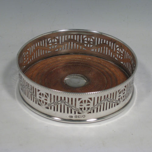 Sterling silver pair of wine bottle table coasters, having round bodies with hand-pierced decoration and engraved swags, with wood-turned bases and silver buttons, and applied beaded borders. Made by Henry Freeman Ltd., of London in 1913. The dimensions of these wine coasters are diameter 13 cms (5 inches), height 4 cms (1.5 inches).