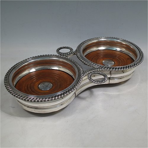 A rare Antique Georgian Old Sheffield plated wine bottle coaster trolley, in a Regency style, having round bellied bodies, with applied gadroon borders, with two stopper side-holders, and with wood-turned bases with silver buttons, all sitting on an oak frame with bone wheels. Made in ca. 1815. The dimensions of this fine hand-made antique wine coaster bottle trolley are diameter of coasters 15 cms (6 inches), and total length 32cms (12.5 inches). Please note that the buttons are crested.   