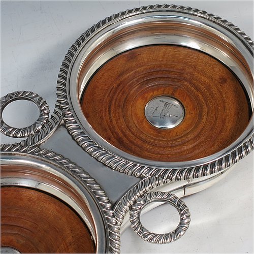 A rare Antique Georgian Old Sheffield plated wine bottle coaster trolley, in a Regency style, having round bellied bodies, with applied gadroon borders, with two stopper side-holders, and with wood-turned bases with silver buttons, all sitting on an oak frame with bone wheels. Made in ca. 1815. The dimensions of this fine hand-made antique wine coaster bottle trolley are diameter of coasters 15 cms (6 inches), and total length 32cms (12.5 inches). Please note that the buttons are crested.   