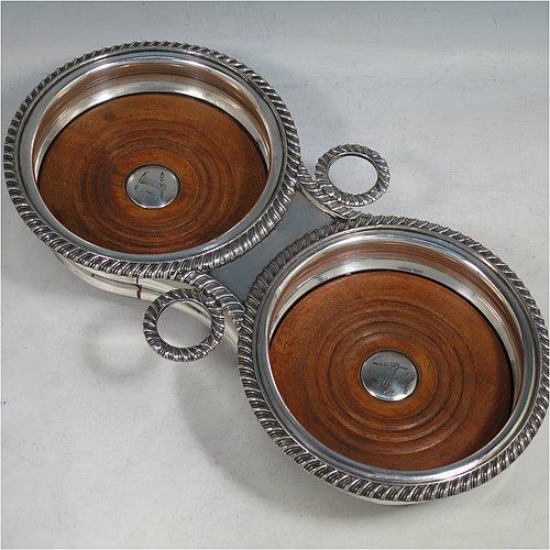 A rare Antique Georgian Old Sheffield plated wine bottle coaster trolley, in a Regency style, having round bellied bodies, with applied gadroon borders, with two stopper side-holders, and with wood-turned bases with silver buttons, all sitting on an oak frame with bone wheels. Made in ca. 1815. The dimensions of this fine hand-made antique wine coaster bottle trolley are diameter of coasters 15 cms (6 inches), and total length 32cms (12.5 inches). Please note that the buttons are crested.   