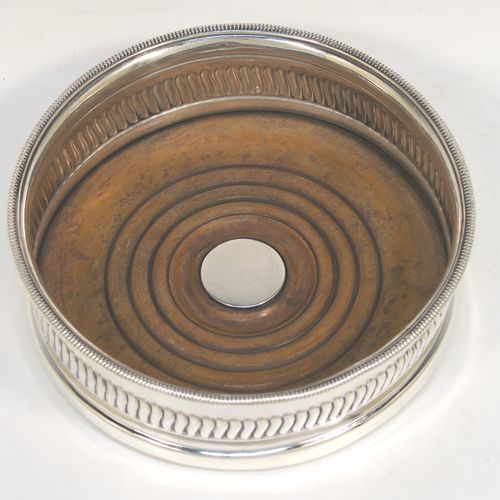 A very handsome Antique Georgian Sterling Silver wine bottle table coaster, in a Regency style, having a round bellied body with a hand-chased band of vertical fluting, an applied rope-twist border, and an oak wood-turned base with central silver button. This elegant antique silver wine bottle coaster was made in Sheffield in 1805. The dimensions of this fine hand-made silver wine bottle coaster are diameter 13 cms (5.25 inches), and height 4.5 cms (1.75 inches).   
