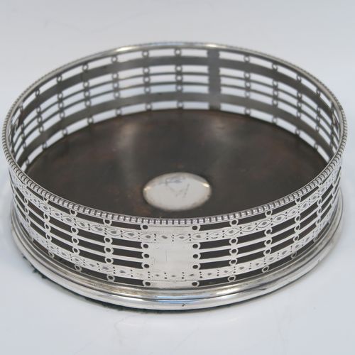 A beautiful and large Antique Georgian Neoclassical style Sterling Silver wine bottle table coaster, having a round hand-pierced body with banded geometrical decoration, together with an applied bead-edged border, and a wood-turned base with silver button. This elegant antique silver wine bottle coaster was made by Edward Lowe of London in 1778. The dimensions of this fine hand-made antique silver wine bottle coaster are diameter 14.5 cms (5.75 inches), and height 4.5 cms (1.75 inches).   