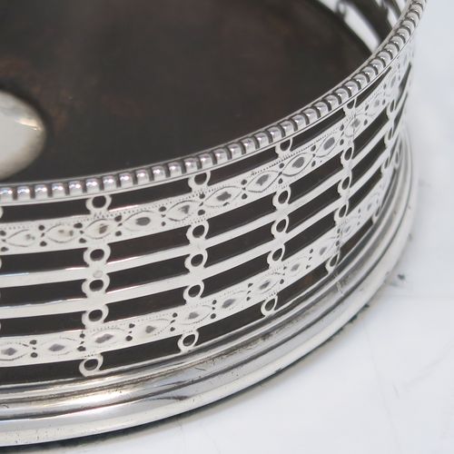 A beautiful and large Antique Georgian Neoclassical style Sterling Silver wine bottle table coaster, having a round hand-pierced body with banded geometrical decoration, together with an applied bead-edged border, and a wood-turned base with silver button. This elegant antique silver wine bottle coaster was made by Edward Lowe of London in 1778. The dimensions of this fine hand-made antique silver wine bottle coaster are diameter 14.5 cms (5.75 inches), and height 4.5 cms (1.75 inches).