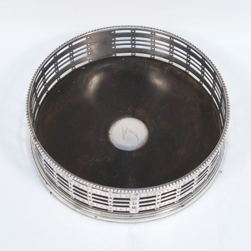 A beautiful and large Antique Georgian Neoclassical style Sterling Silver wine bottle table coaster, having a round hand-pierced body with banded geometrical decoration, together with an applied bead-edged border, and a wood-turned base with silver button. This elegant antique silver wine bottle coaster was made by Edward Lowe of London in 1778. The dimensions of this fine hand-made antique silver wine bottle coaster are diameter 14.5 cms (5.75 inches), and height 4.5 cms (1.75 inches).