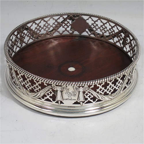 An Antique Georgian Neoclassical style Sterling Silver wine bottle table coaster, having a round hand-pierced body, with applied ribbons and swags on a hand-pierced body, together with an applied rope-twist or gadroon border, and a wood-turned base with bone button. Made by Elizabeth Jones of London in 1774. The dimensions of this fine hand-made antique silver wine bottle coaster are diameter 11 cms (4.3 inches), and height 3.5 cms (1.3 inches).   
