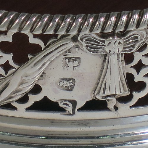 An Antique Georgian Neoclassical style Sterling Silver wine bottle table coaster, having a round hand-pierced body, with applied ribbons and swags on a hand-pierced body, together with an applied rope-twist or gadroon border, and a wood-turned base with bone button. Made by Elizabeth Jones of London in 1774. The dimensions of this fine hand-made antique silver wine bottle coaster are diameter 11 cms (4.3 inches), and height 3.5 cms (1.3 inches).